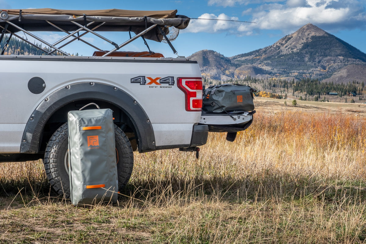 Fishpond Backroad Large Rolling Duffel - Overcast Grey, standing beside a pickup truck