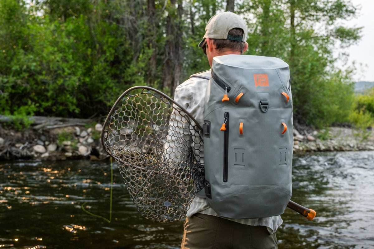 Fishpond Thunderhead HD Backpack, Overcast Grey, worn by angler wading with net