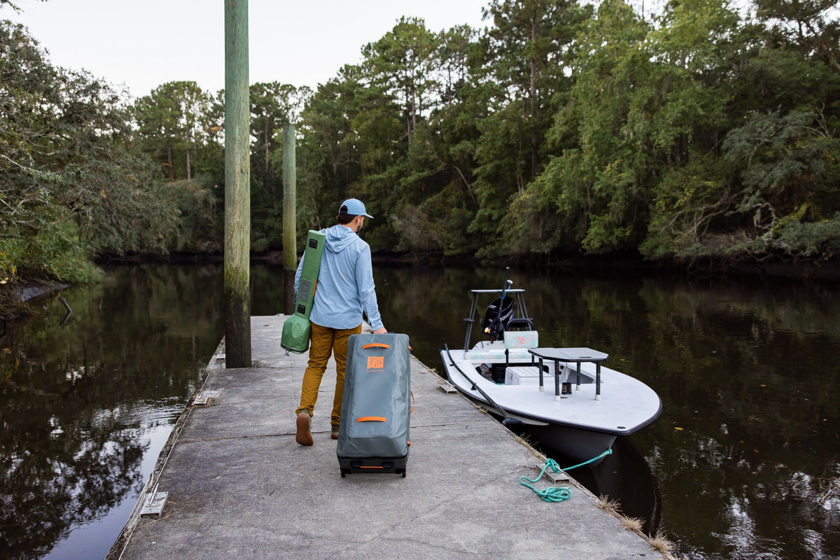 Fishpond Backroad Large Rolling Duffel - Overcast Grey, being rolled down a dock toward a boat