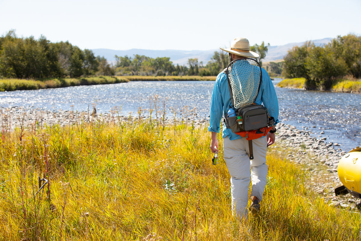 Guy Walking To The River Wearing Fishpond Waterdance Pro Guide Pack - Driftwood